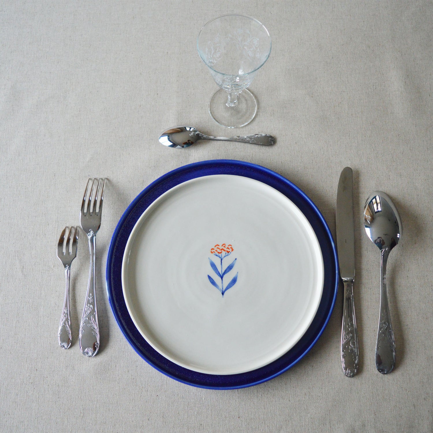 Porcelaine fabriquée en France, assiette à dessert Flora sur assiette bleue Primavera avec couverts Degrenne