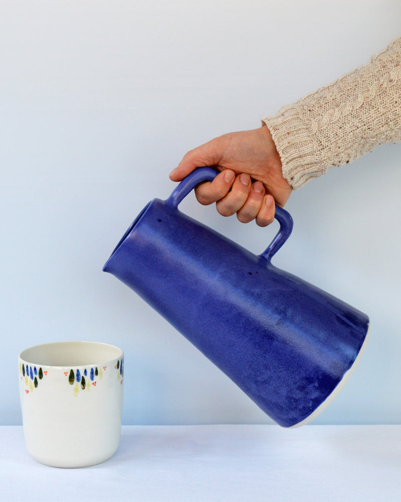 Porcelaine fabriquée en France, carafe bleu Primavera versée vers une tasse à thé à motif Primavera
