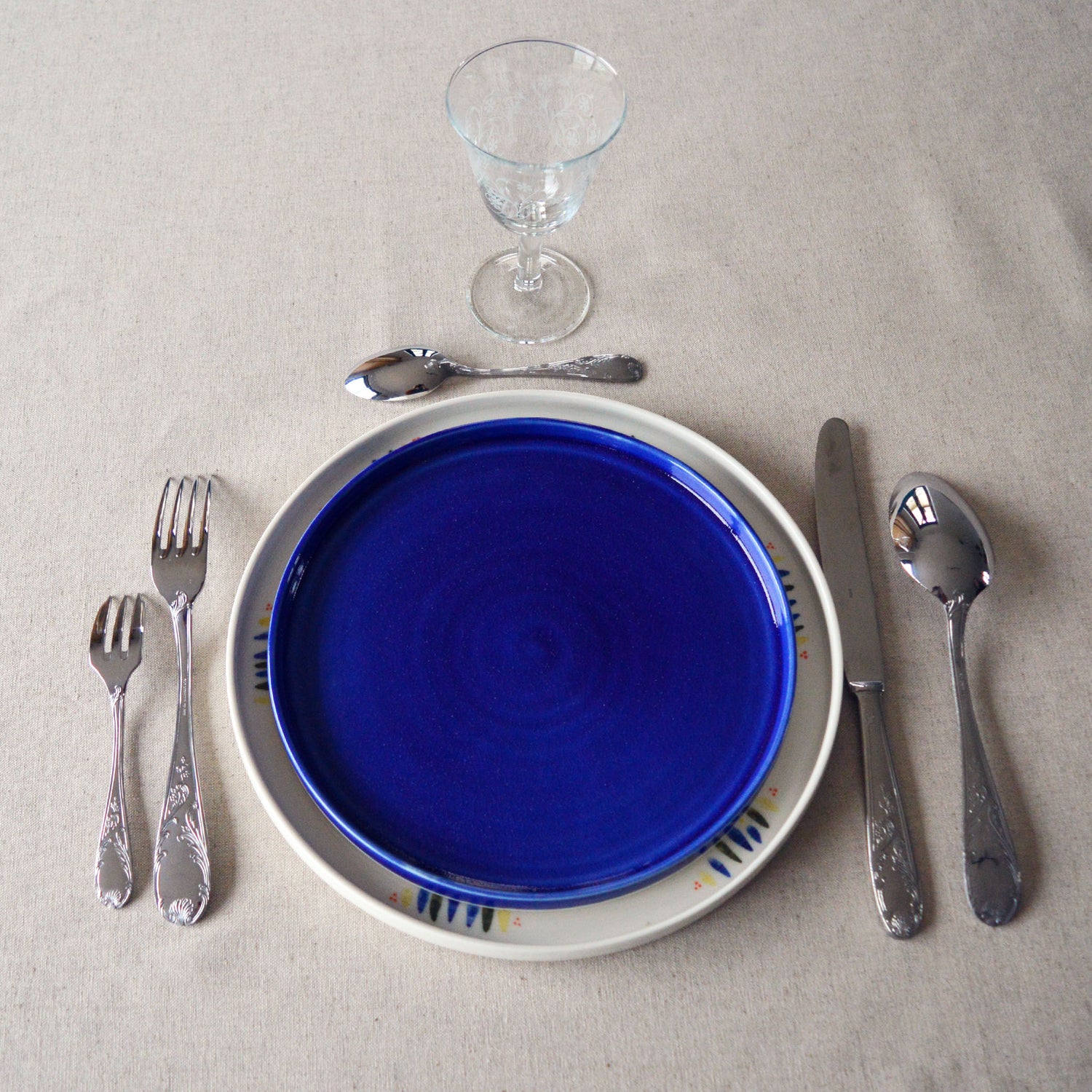 Porcelaine fabriquée en France, assiette à dessert bleue sur une grande assiette à motif Primavera, couverts chinés Degrenne et verre