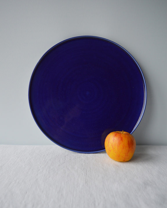 Porcelaine fabriquée en France, plat de service bleu sur fond blanc à côté d'une pomme