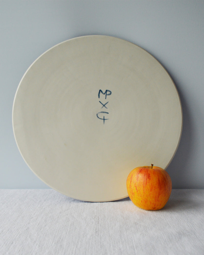 Porcelaine fabriquée en France, dos d'un plat de service sur fond blanc à côté d'une pomme