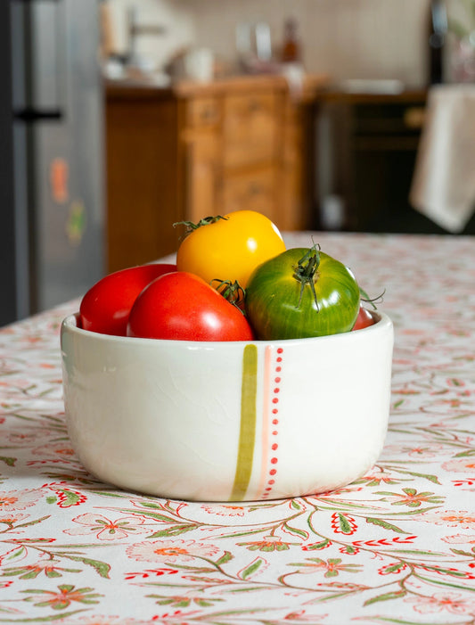 Saladier en porcelaine artisanal fabriqué en France, motif de rayures vertes, roses et rouges, rempli de tomates, sur nappe à motif floral