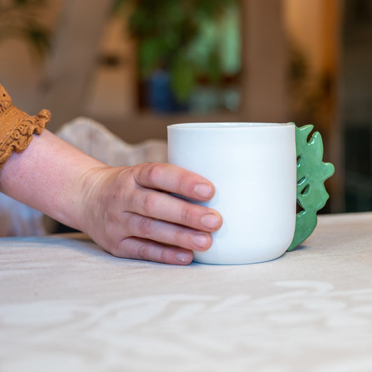 Tasse à thé blanche en porcelaine, fabriquée en France, avec anse verte motif cœur alsacien, tenue à la main