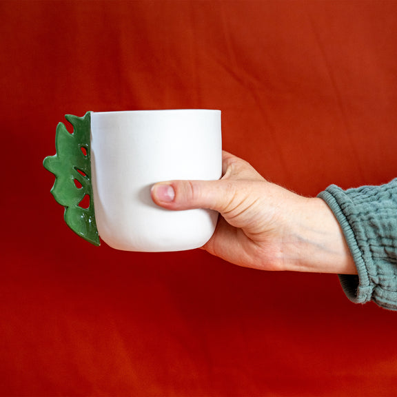 Tasse à thé blanche en porcelaine, fabriquée en France, avec anse verte motif cœur alsacien, tenue à la main