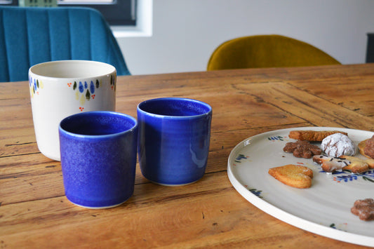 Porcelaine artisanale fabriquée en France, tasses à café bleues et tasse à thé motif Primavera, plat rond motif Primavera sur table en bois.