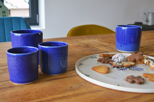 Porcelaine artisanale fabriquée en France, tasses à thé et à café bleues Maison Primavera, à côté d'un plat à motif Primavera, sur une table en bois.