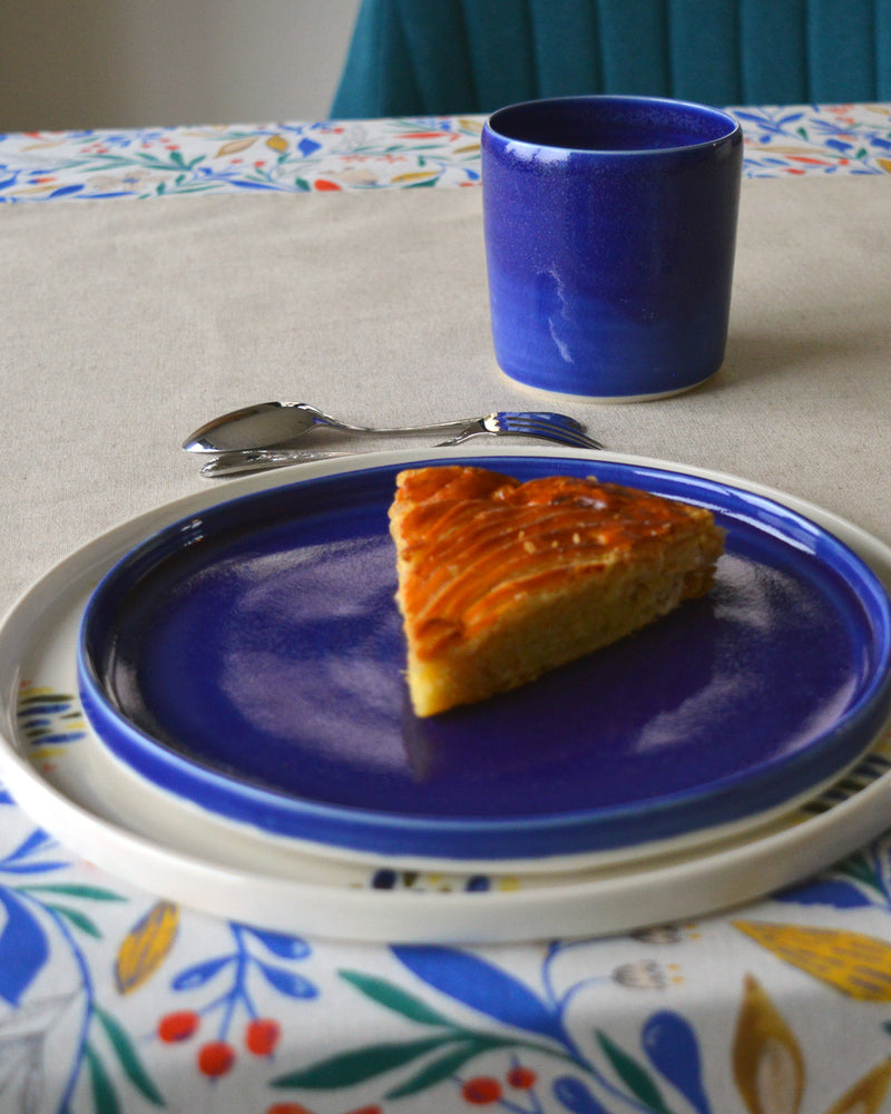 Porcelaine artisanale fabriquée en France, tasse à thé bleue Maison Primavera avec assiettes à motif et bleue sur linge de table français.