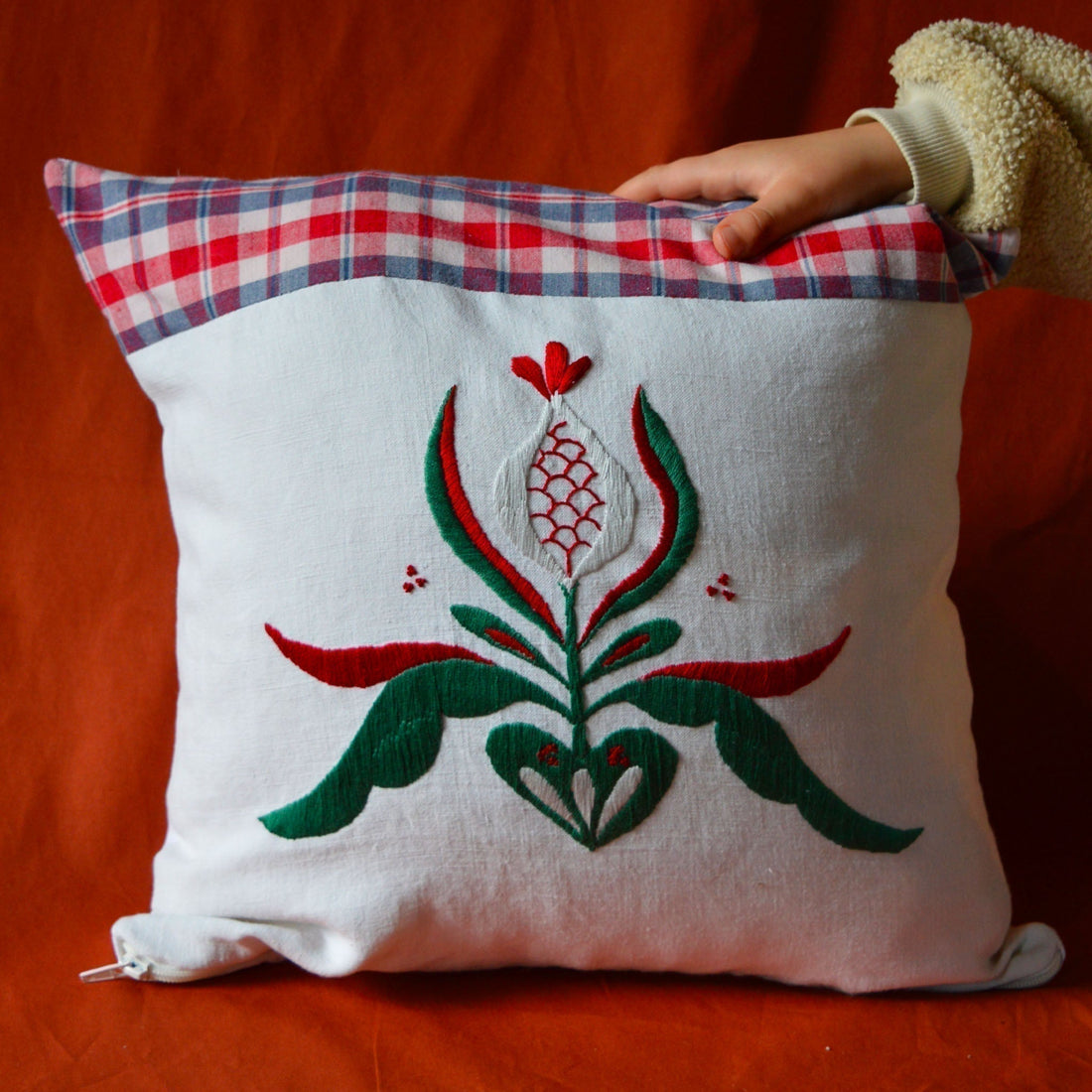 Coussin brodé à la main, avec un mélange de kelsch et de fils de coton, dans les teintes vertes et rouge et un fond blanc.