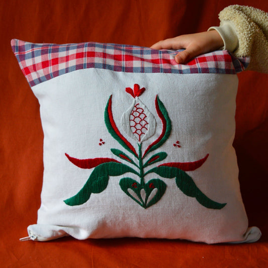 Coussin brodé à la main, avec un mélange de kelsch et de fils de coton, dans les teintes vertes et rouge et un fond blanc.