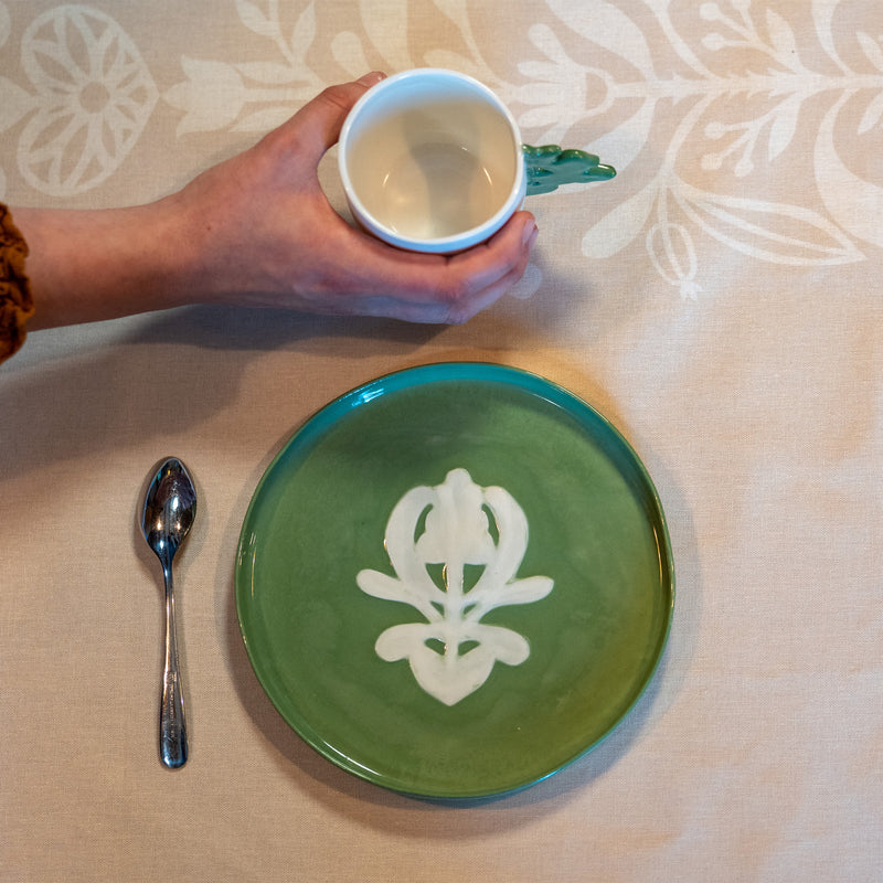 Assiette à dessert verte à motif blanc, en porcelaine, fabriquée en France artisanalement, motif arbre de vie alsacien, sur nappe beige à motif made in France