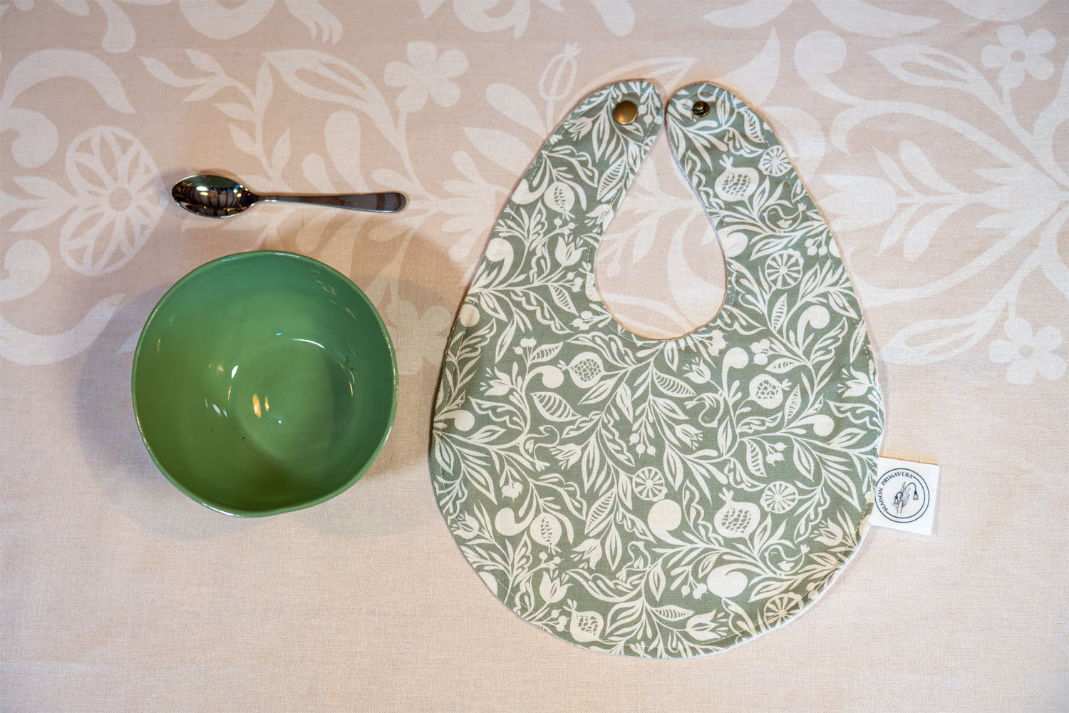 Bavoir vert et blanc fabriqué en France, en coton et en lin, avec motif floral, polychrome alsacien, bol vert en porcelaine, nappe beige