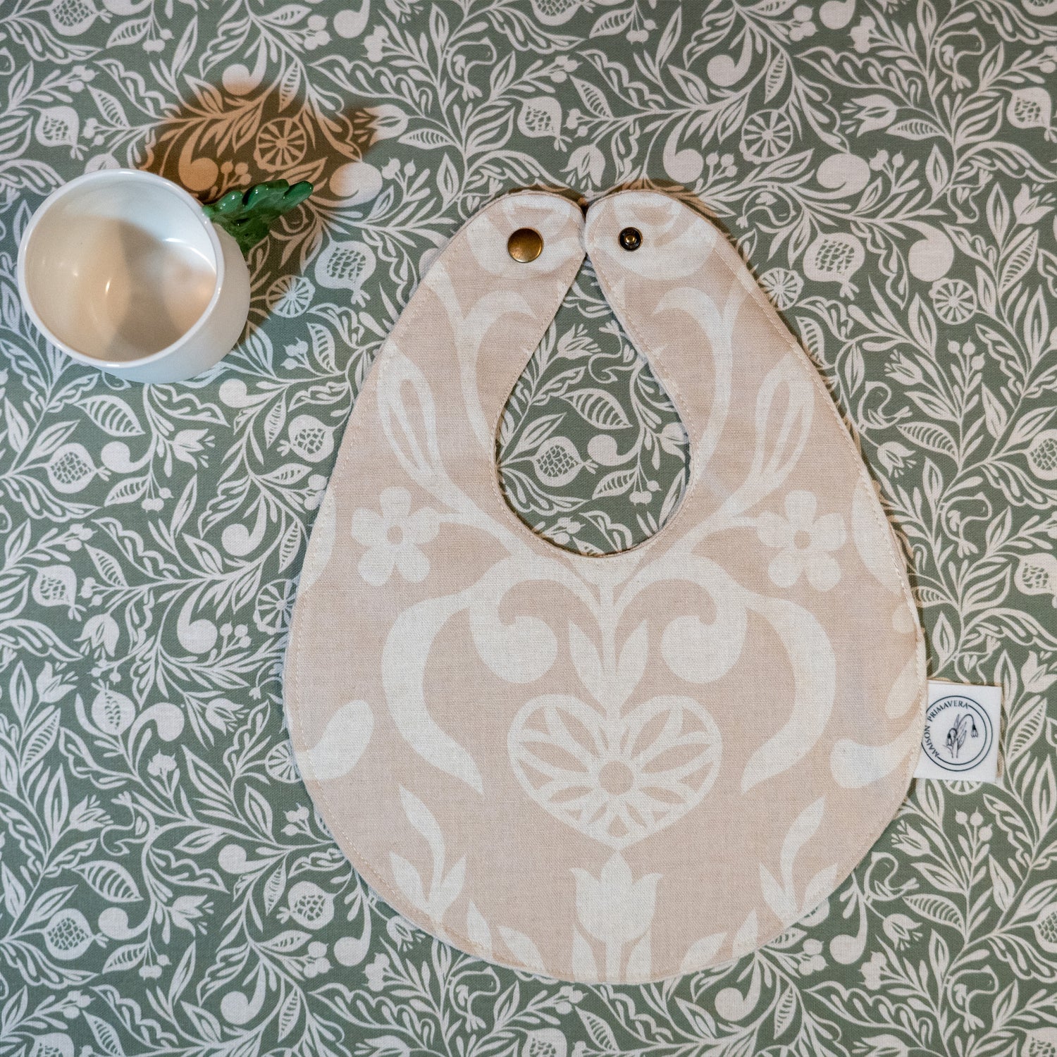 Bavoir beige et blanc fabriqué en France, en coton et en lin, avec motif floral, arbre de vie alsacien, nappe verte motif floral, tasse en porcelaine artisanale