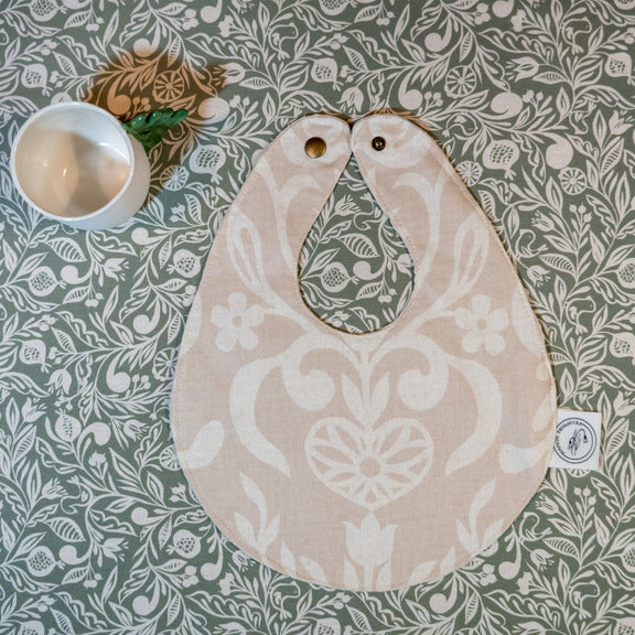 Bavoir beige et blanc fabriqué en France, en coton et en lin, avec motif floral, arbre de vie alsacien, nappe verte motif floral, tasse en porcelaine artisanale