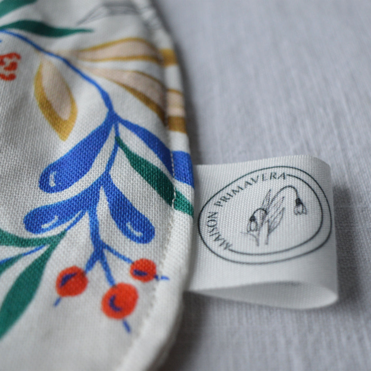 Etiquette du bavoir en coton et lin à motif Primavera, tissé et fabriqué en France, sur fond blanc