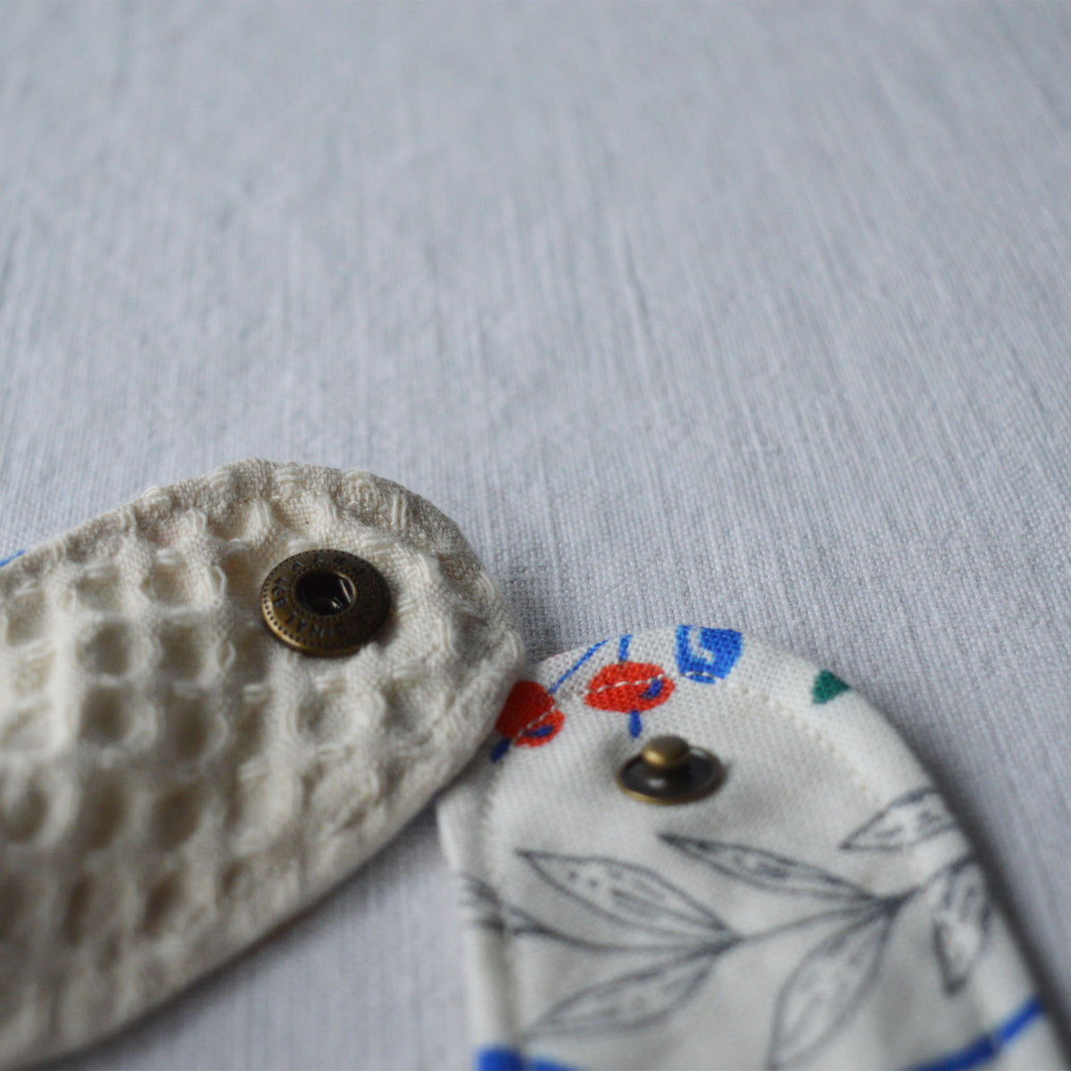 Bouton ouvert du bavoir en coton et lin à motif Primavera, tissé et fabriqué en France, sur fond blanc