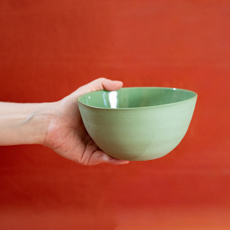 Bol vert en porcelaine, fabriqué en France, artisanal, tenu à une main, fond orange