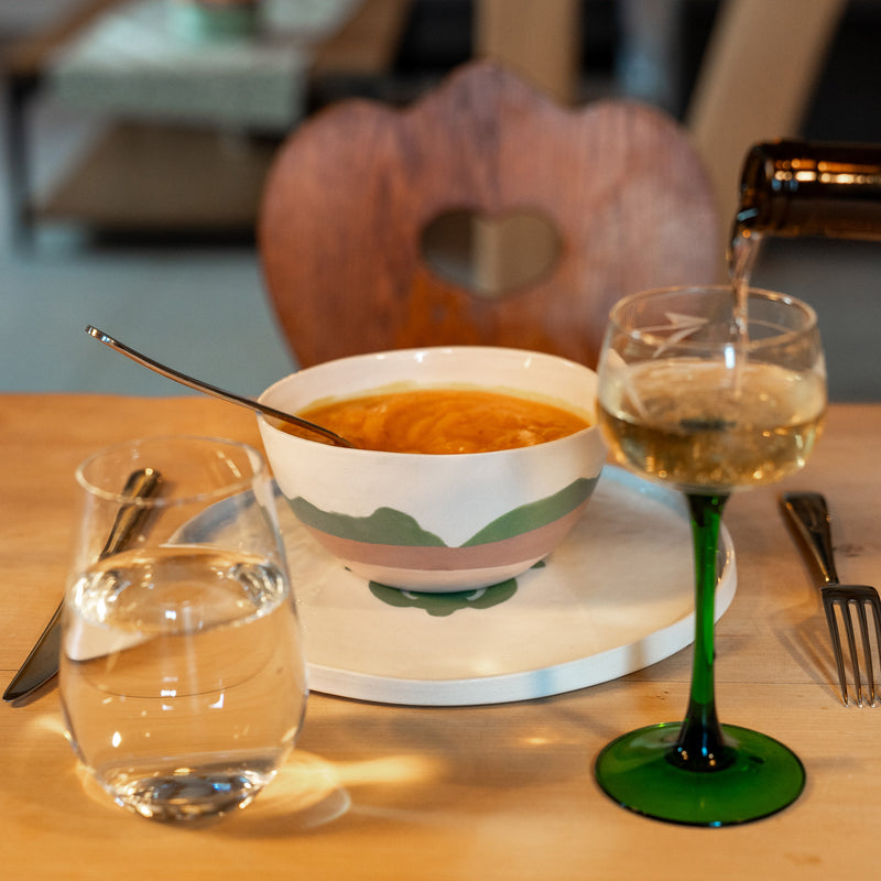 Bol en porcelaine fabriqué en France, artisanal, motif de montagnes, des Vosges, couleurs douces, rempli de soupe avec verre à vin sur table en bois