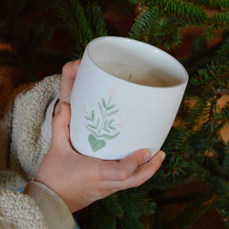 Bougie artisanale coulée dans une tasse à thé en porcelaine, fabriquée en France, senteur de Noël, décor unique Alsace, tenue par mains d'enfant