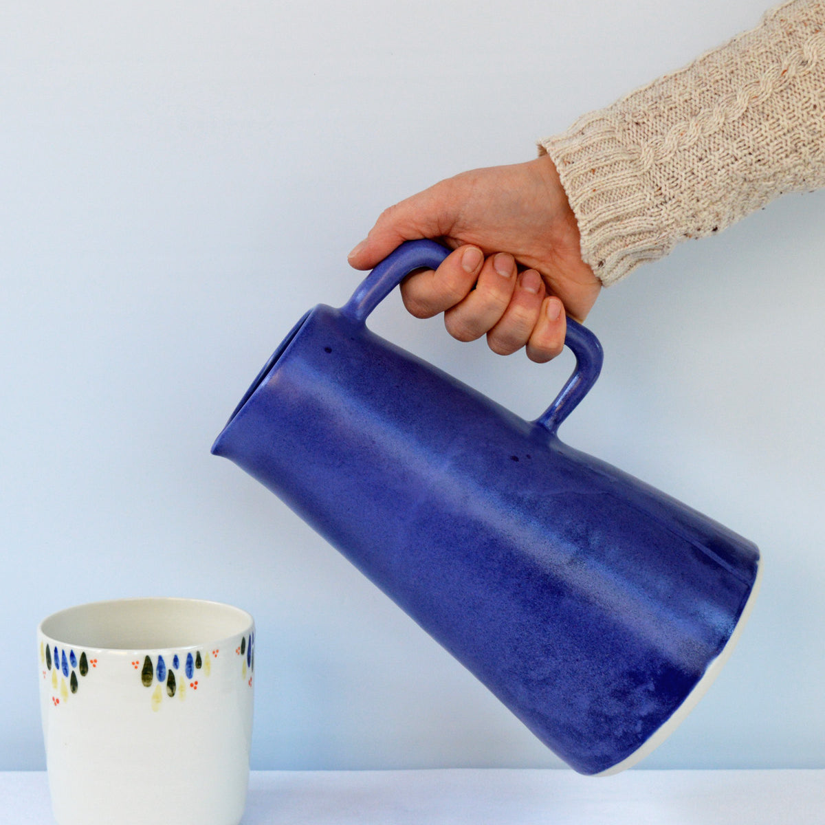 Porcelaine fabriquée en France, carafe bleu Primavera versée vers une tasse à thé à motif Primavera