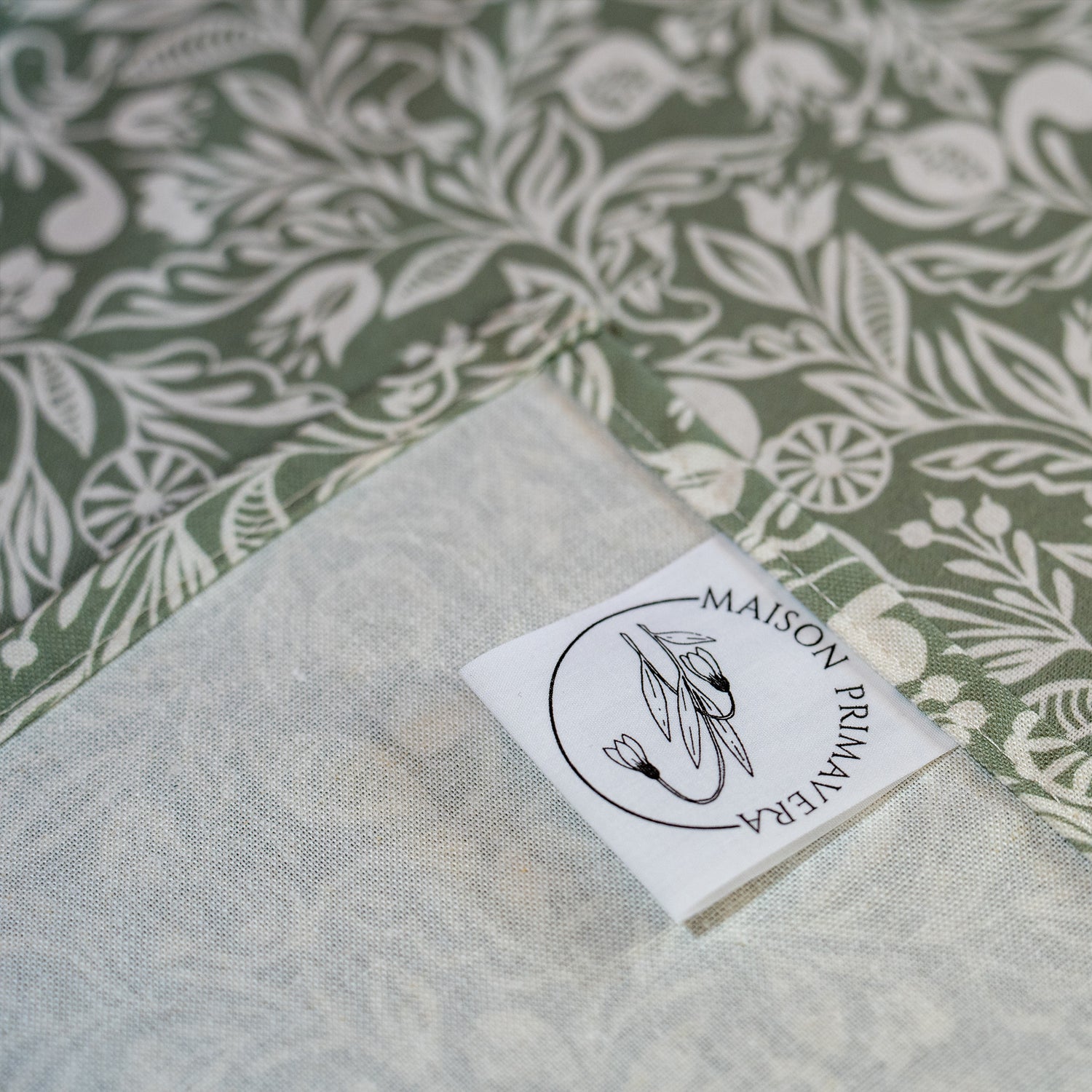 Détail étiquette de chemin de table fabriqué en France, vert et blanc, en coton et lin, motif floral polychrome alsacien
