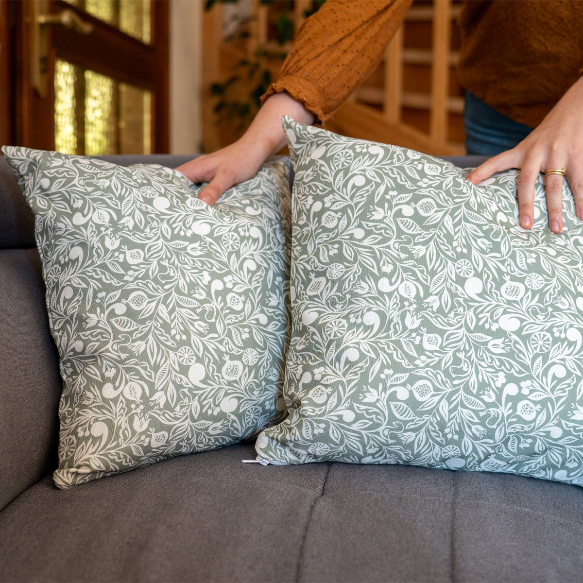 2 coussins verts et blancs fabriqués en France, en coton et lin, motif floral polychrome alsacien, fermeture zip, sur un canapé gris