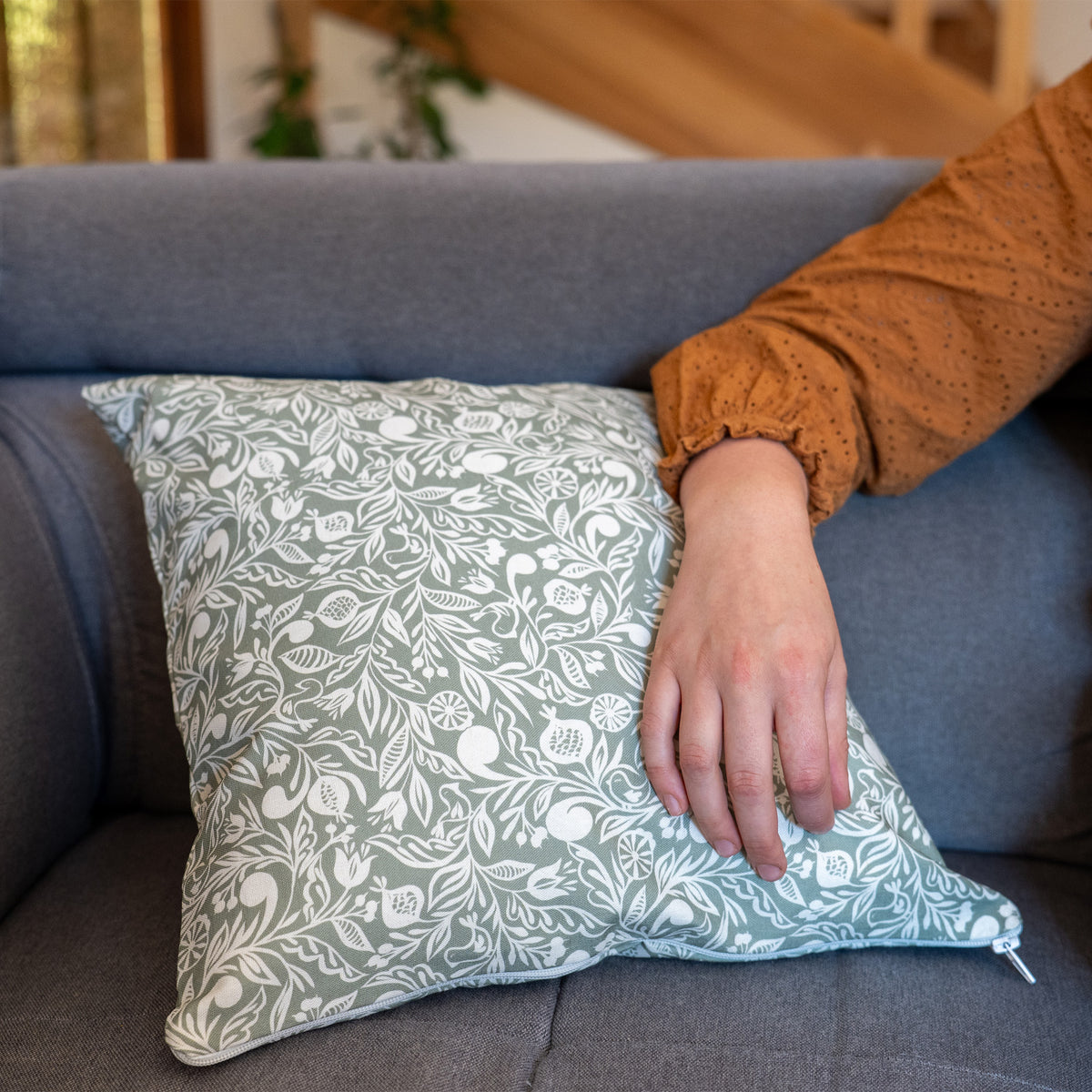 Coussin vert et blanc fabriqué en France, en coton et lin, motif floral polychrome alsacien, sur canapé avec bras posé dessus