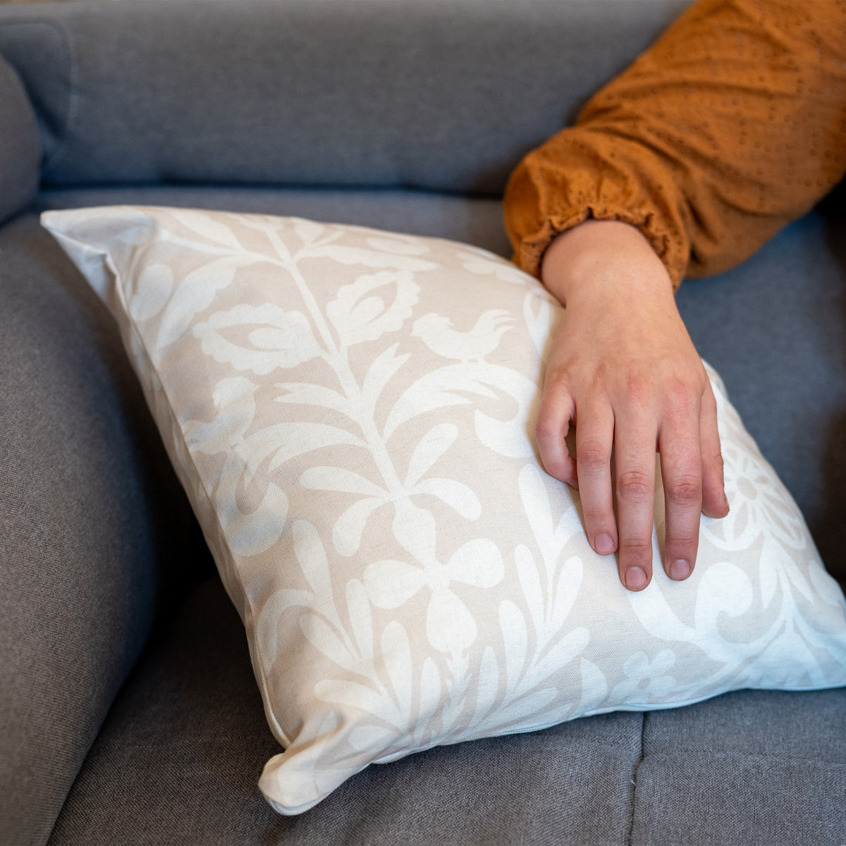 Coussin beige et blanc fabriqué en France, en coton et lin, motif floral arbre de vie Alsace, fermeture zip, avec bras posé dessus