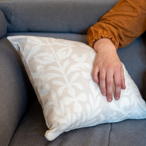 Coussin beige et blanc fabriqué en France, en coton et lin, motif floral arbre de vie Alsace, fermeture zip, avec bras posé dessus