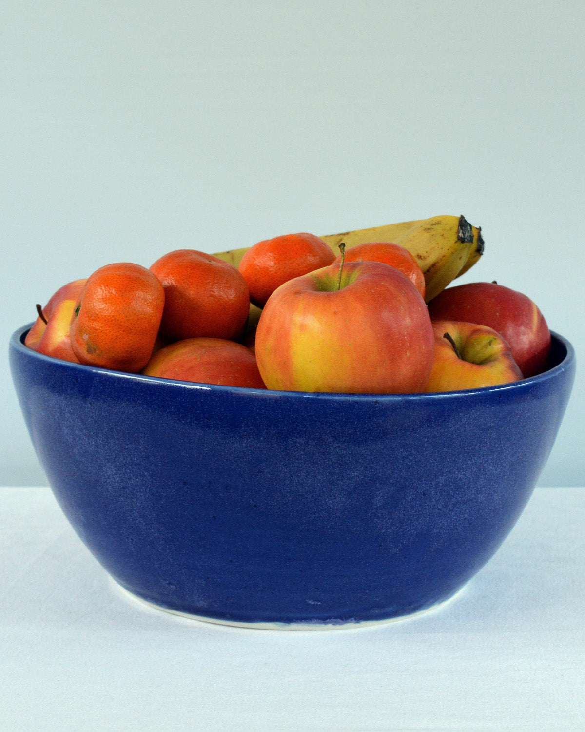 Porcelaine fabriquée en France, grand saladier bleu Primavera rempli de fruits sur fond blanc