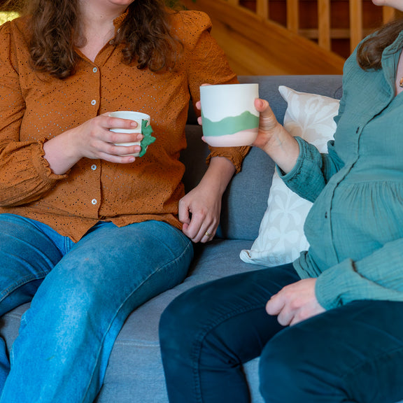 Tasses en porcelaine fabriquées en France à la main, motif paysage Alsace et cœur alsacien, tenues par deux femmes