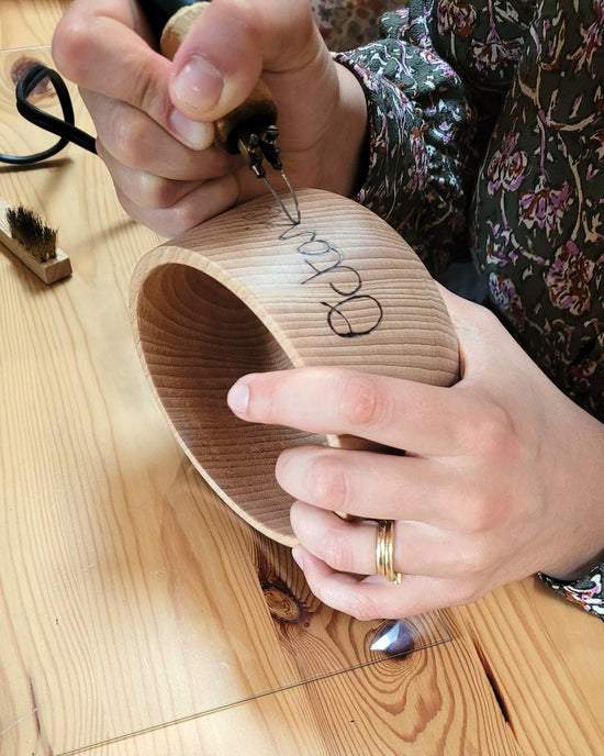 Pyrogravure à la main d'un prénom d'enfant sur un bol en bois fabriqué en France.