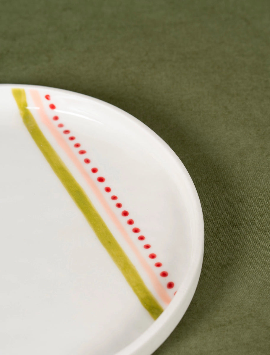 Zoom sur assiette à dessert en porcelaine artisanale fabriquée en France, motif rayures vertes, roses et rouges