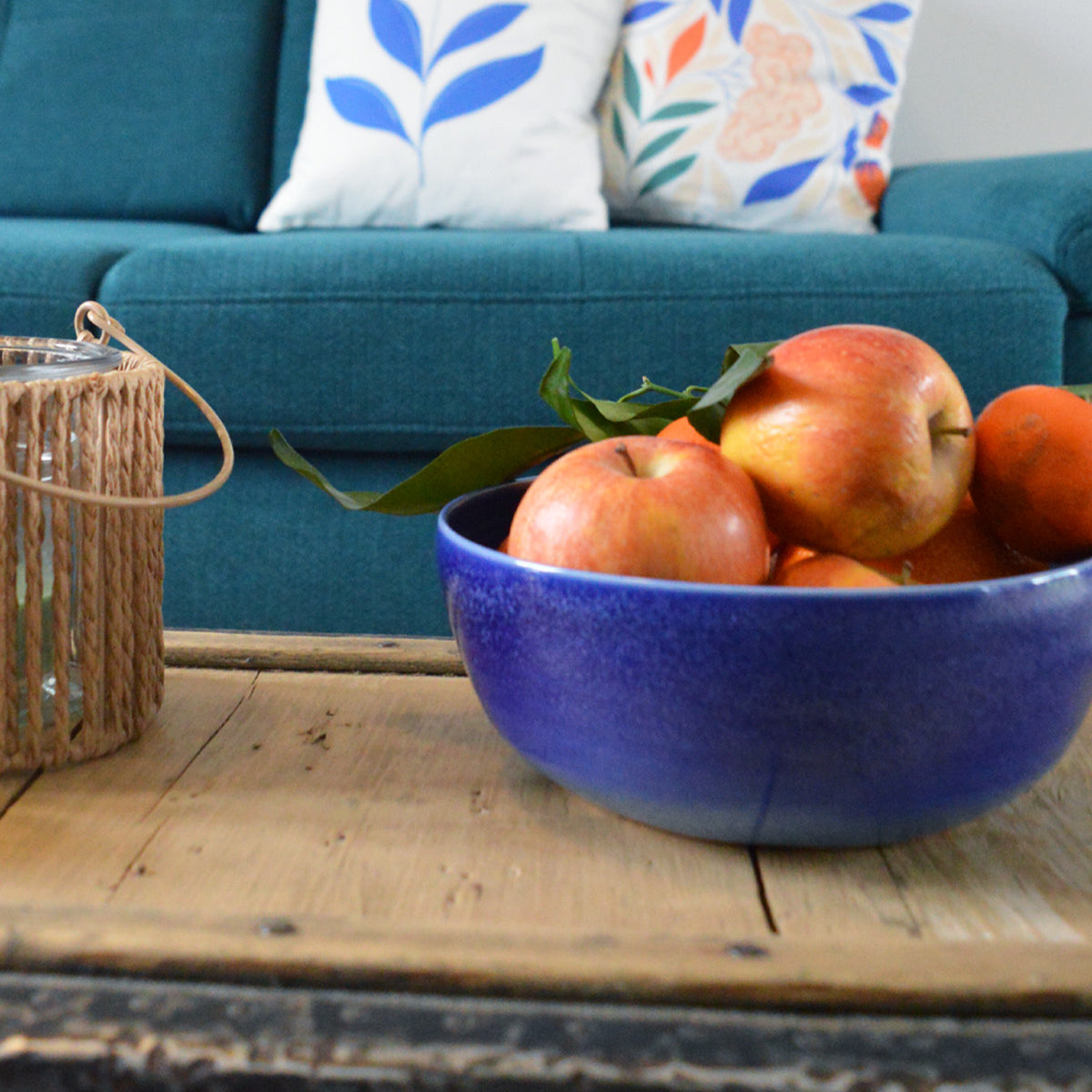 Porcelaine fabriquée en France, petit saladier bleu rempli de fruits sur table basse avec des coussins Primavera dans le fond