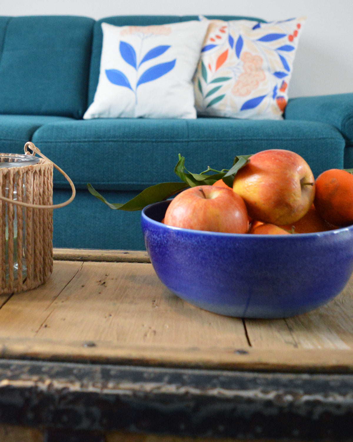 Porcelaine fabriquée en France, petit saladier bleu rempli de fruits sur table basse avec des coussins Primavera dans le fond