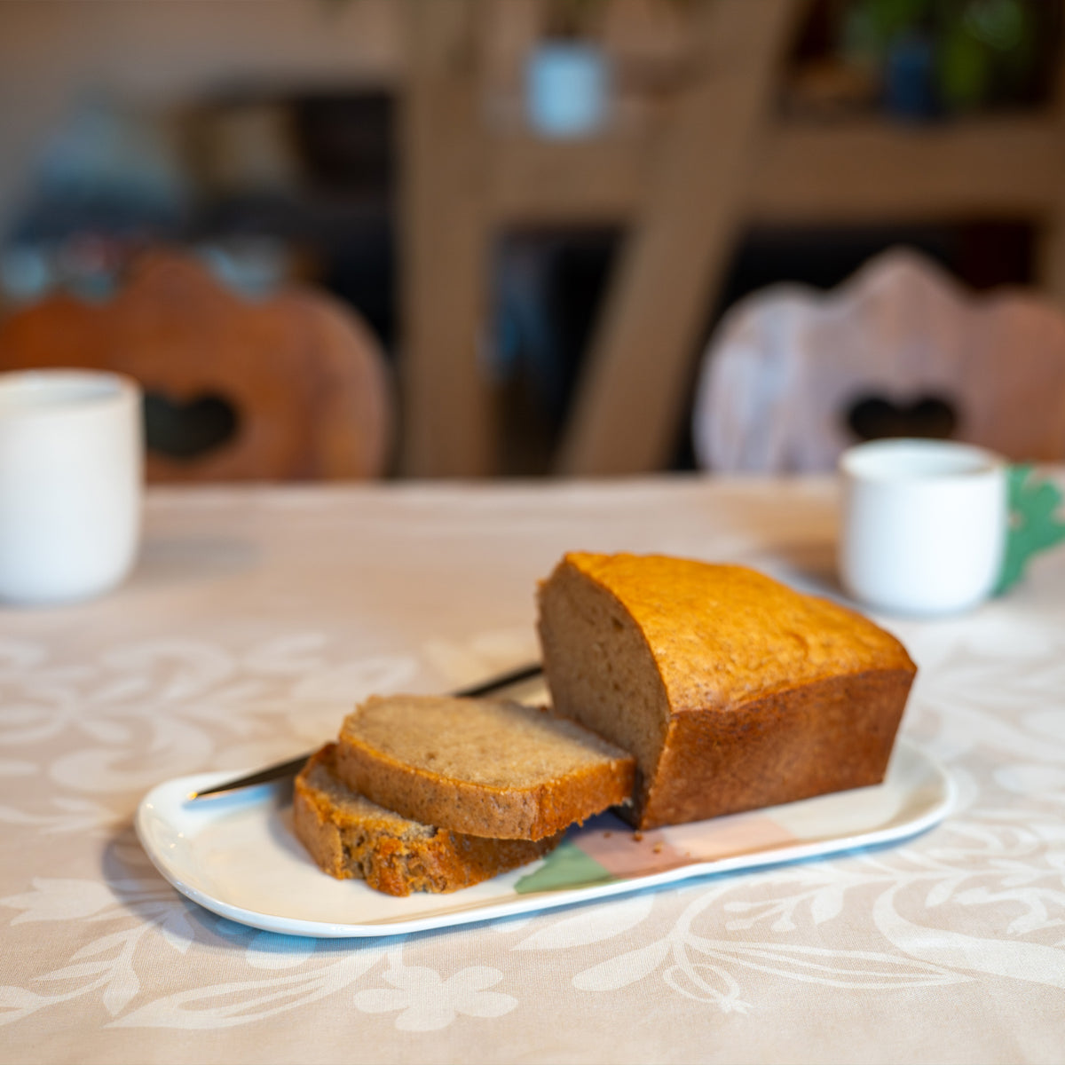 Plat à cake en porcelaine, fabriqué en France, artisanal, blanc à motif de montagne, couleurs pastels, gâteau aux épices tranché sur table dressée