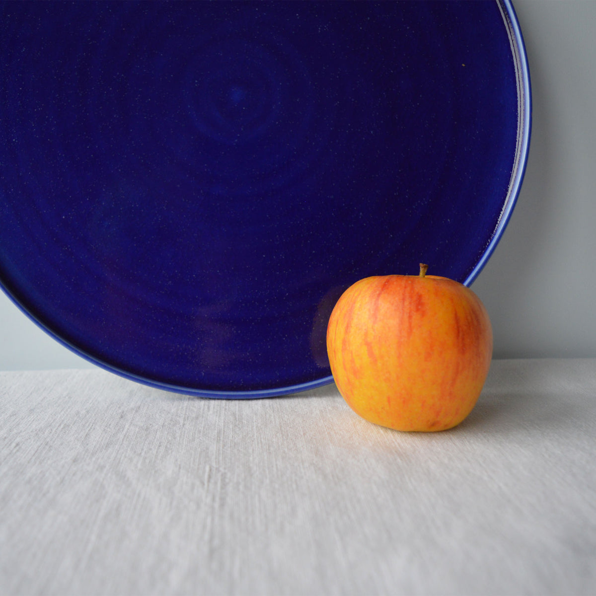 Porcelaine fabriquée en France, zoom sur plat de service bleu sur fond blanc à côté d'une pomme