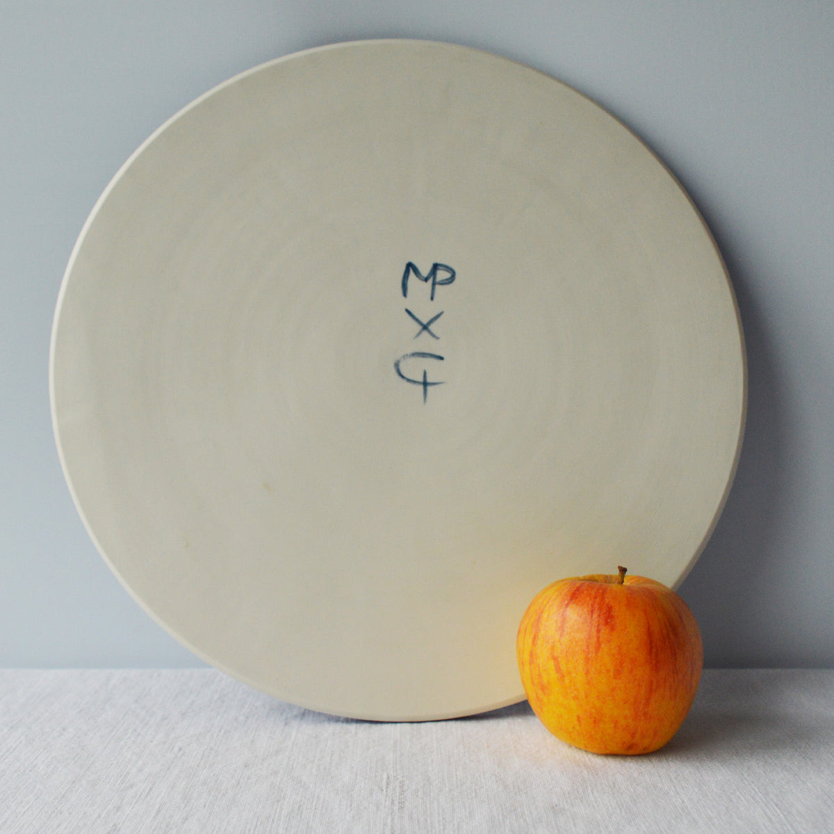 Porcelaine fabriquée en France, dos d'un plat de service sur fond blanc à côté d'une pomme