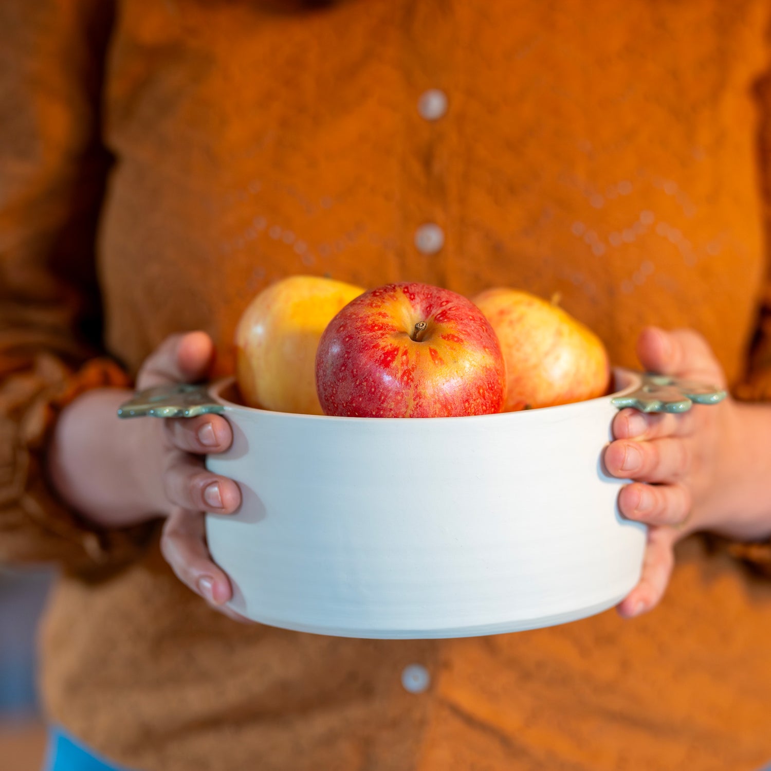Saladier fabriqué en France en porcelaine, artisanal, avec deux anses vertes motif cœur alsacien, rempli de pommes et tenu à deux mains
