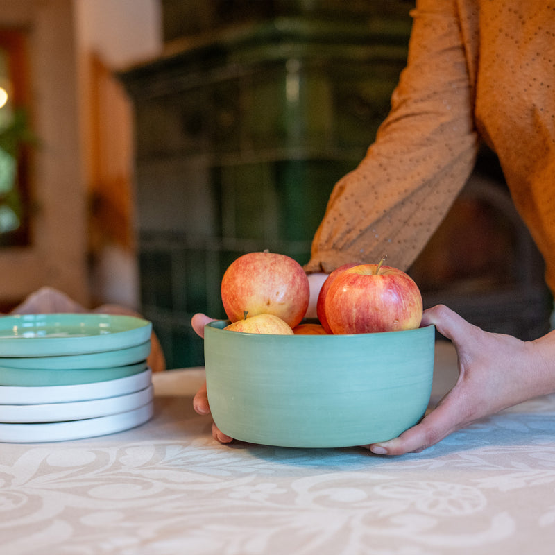 Saladier vert fabriqué en France en porcelaine, artisanal, rempli de pommes sur table dressée avec nappe made in France