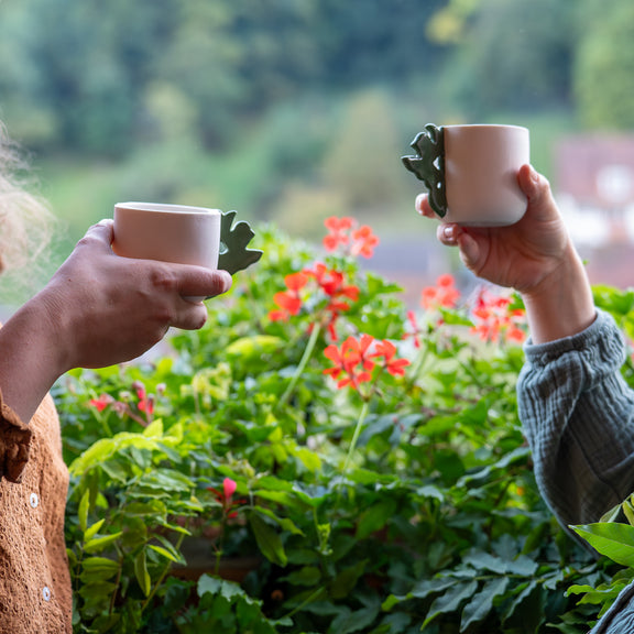 2 tasses à café artisanales fabriquées en France, en porcelaine blanche avec une anse verte motif cœur alsacien, tenues à la main