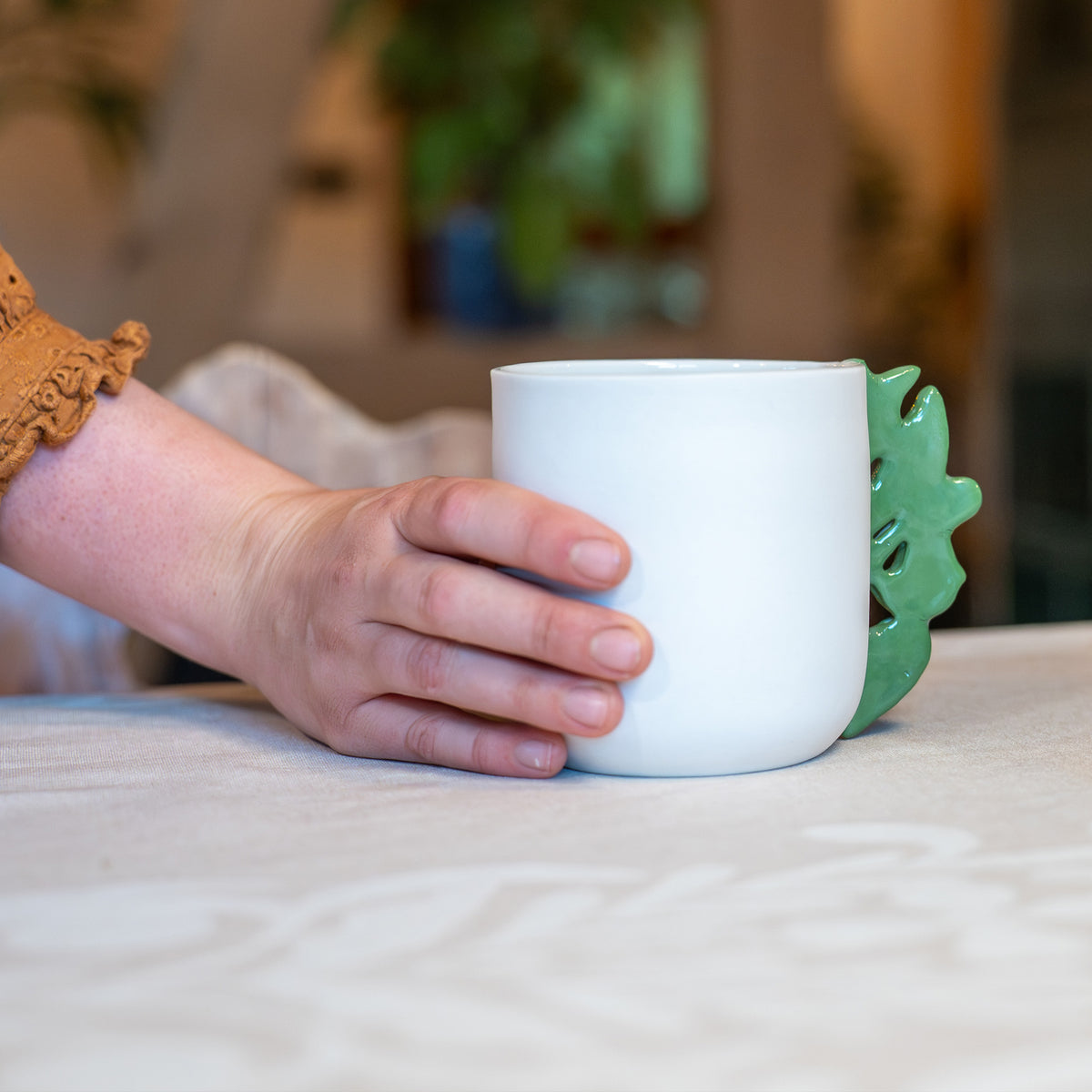Tasse à thé blanche en porcelaine, fabriquée en France, avec anse verte motif cœur alsacien, tenue à la main