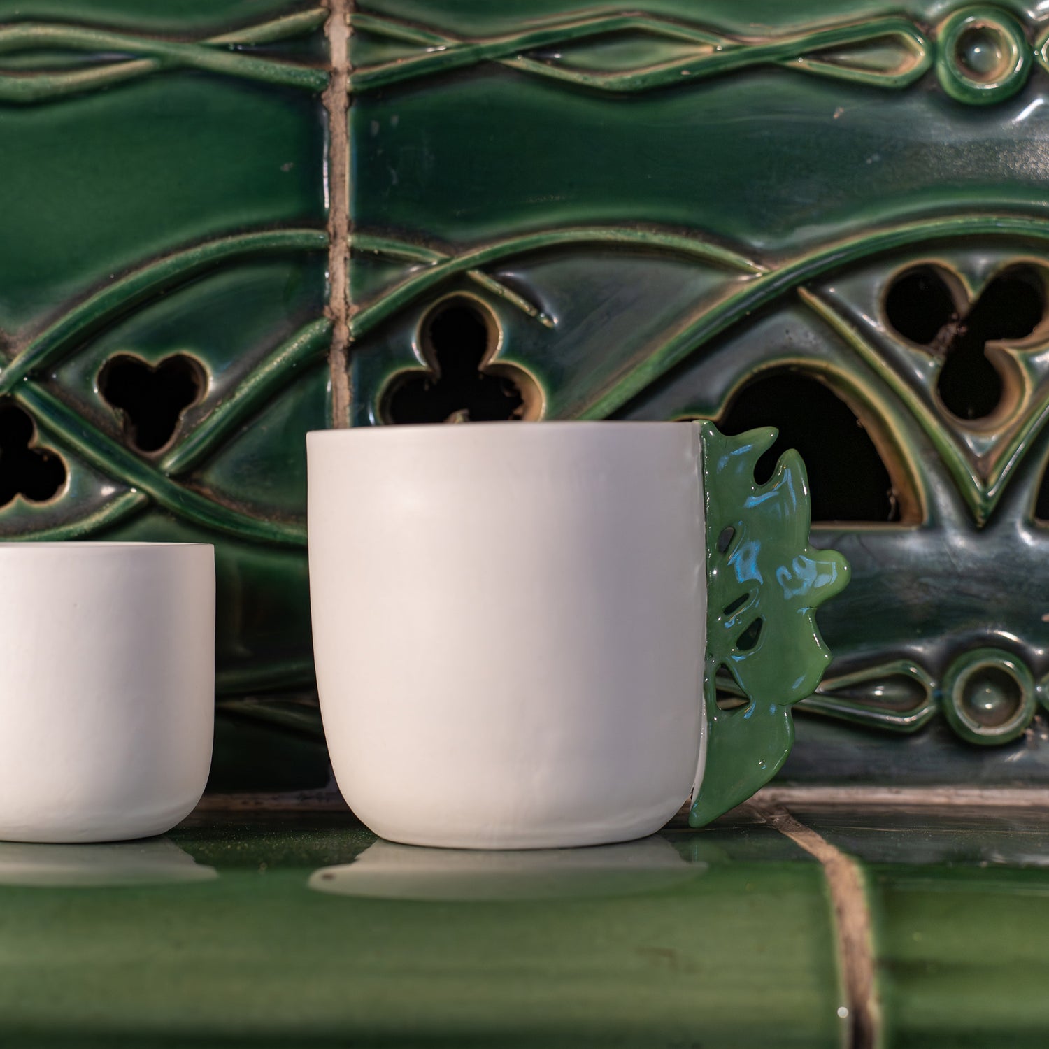 Tasse à thé blanche en porcelaine, fabriquée en France, avec anse verte motif cœur alsacien, posée sur un kachelofe