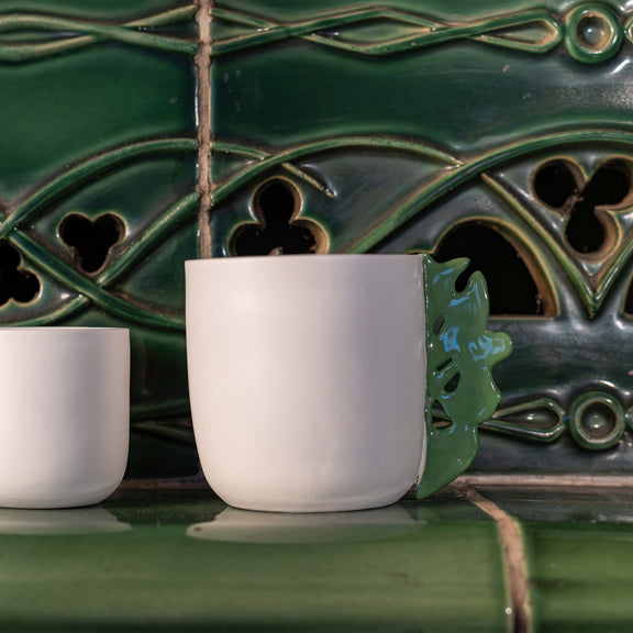 Tasse à thé blanche en porcelaine, fabriquée en France, avec anse verte motif cœur alsacien, posée sur un kachelofe