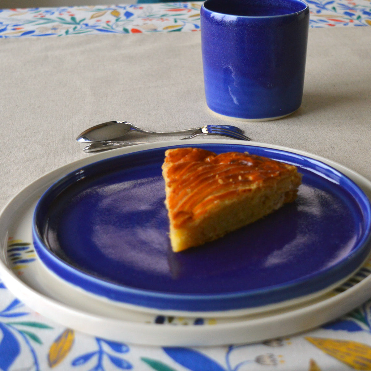 Porcelaine artisanale fabriquée en France, tasse à thé bleue Maison Primavera avec assiettes à motif et bleue sur linge de table français.